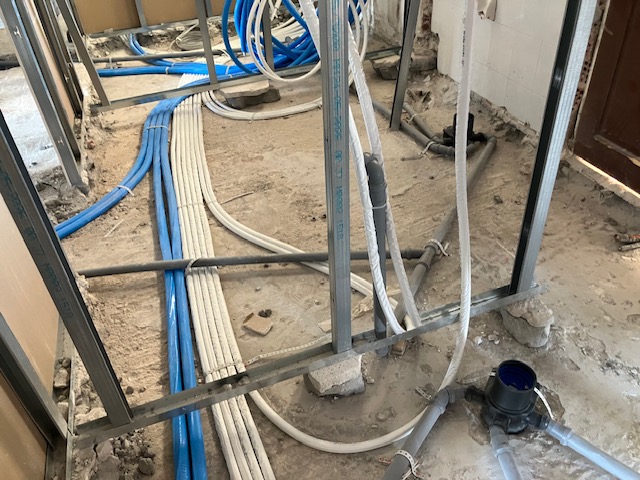 Plumbing and electrical conduits laid across the floor between partition tracks.