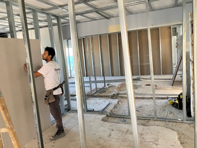 Worker positioning a plasterboard panel against the partition framing.