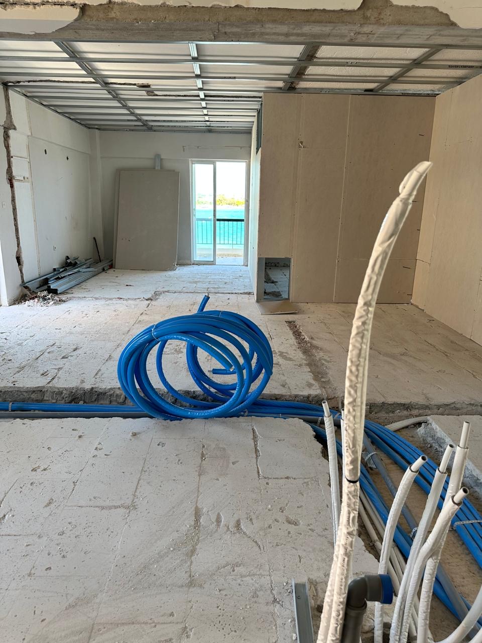 Detail of service pipework crossing the floor slab, with a balcony opening onto the sea beyond.