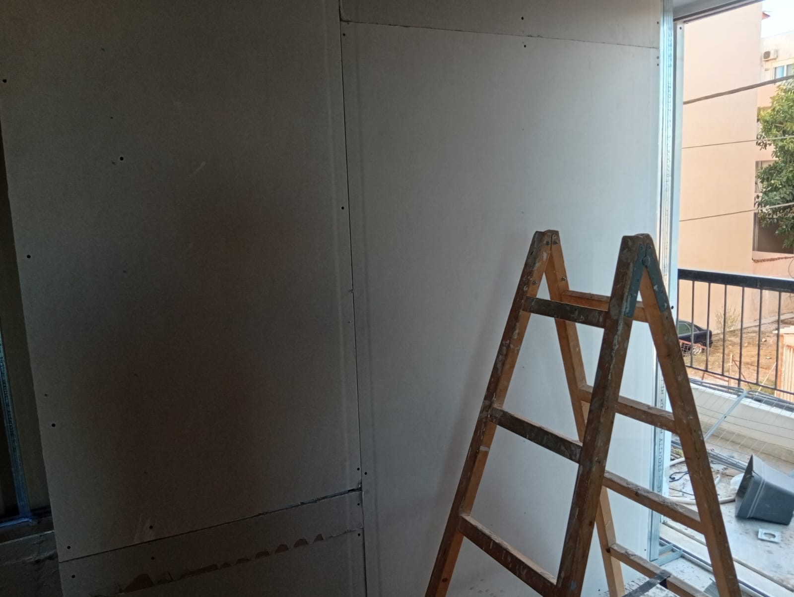 Plasterboard walls closed up beside a balcony opening, with a stepladder in place.