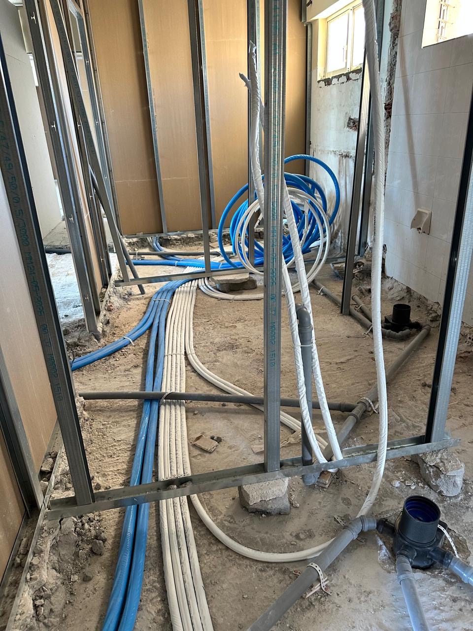 Blue and white service conduits routed along the floor between metal partition studs.