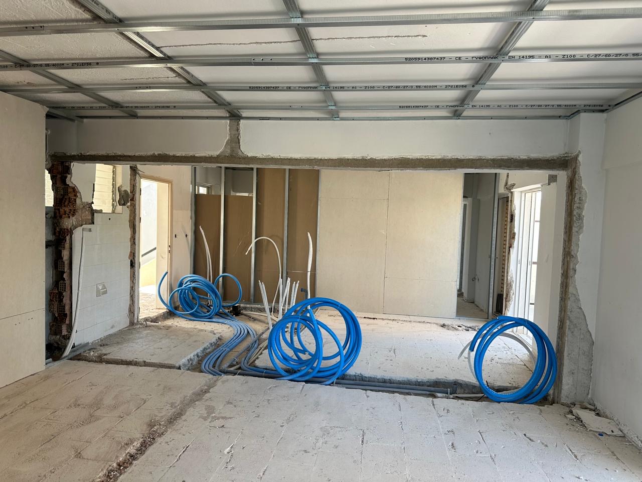 Coils of blue service piping laid out in a room with plasterboard partitions and ceiling framework.