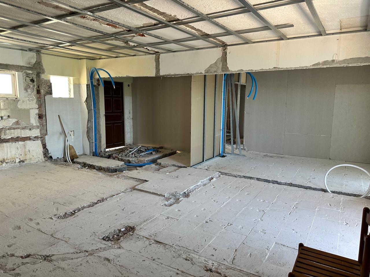 Interior with ceiling framework, new partition studs and service conduits running to an existing entrance door.