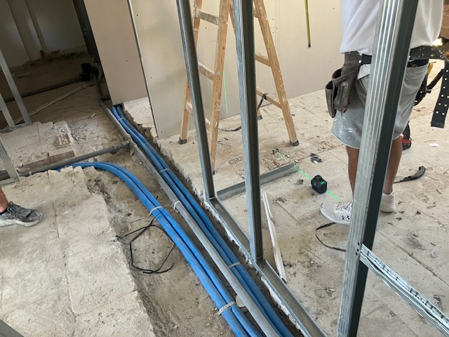 Active first-floor site work beside routed blue building-services pipework and partition framing.