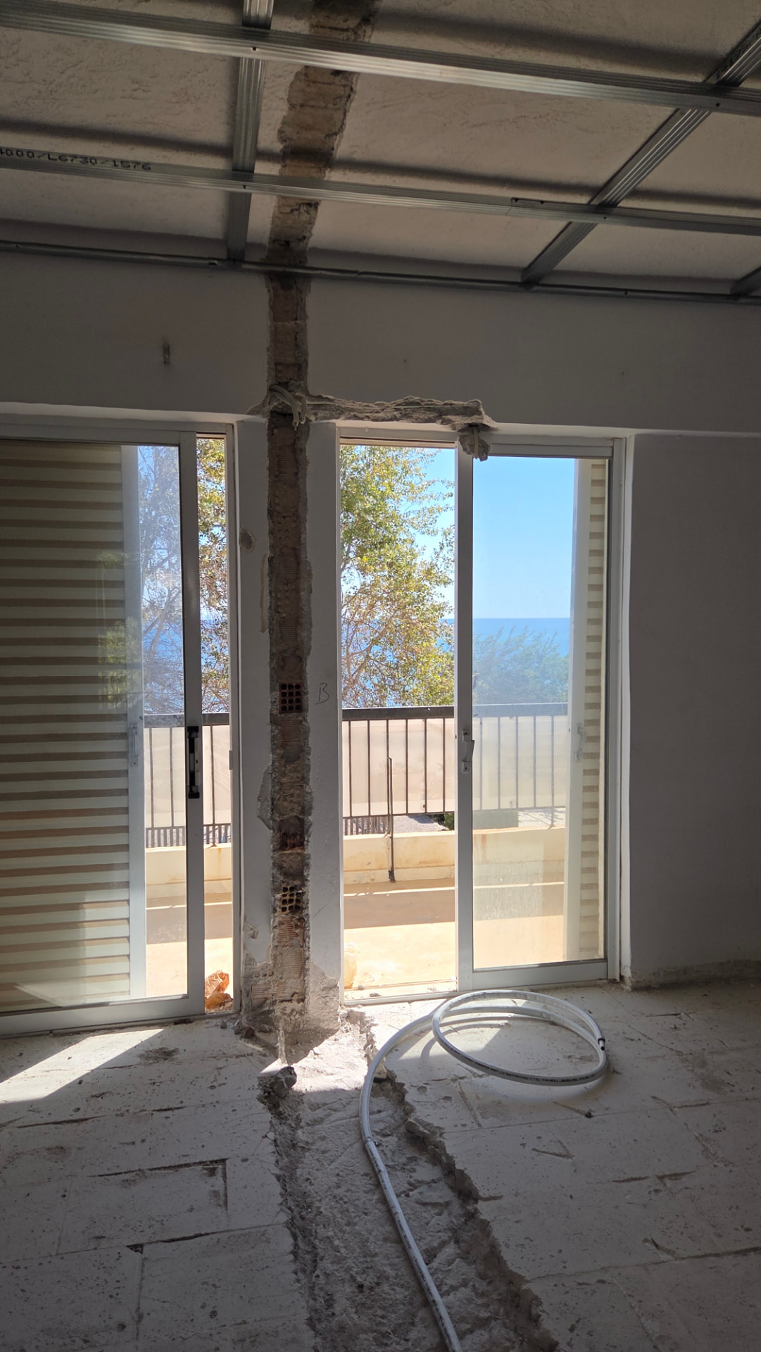Interior construction with exposed ceiling framework, a wall channel and floor routing beside a sea-facing balcony.